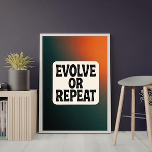 Op de afbeelding: Een ingelijste print met de tekst "EVOLVE OR REPEAT" in zwart op een crème achtergrond. De print heeft een verloop van oranje, groen en zwart. Het kunstwerk wordt getoond op een witte muur, met een houten kruk en plant.