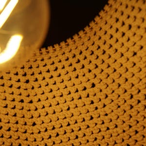 Op de afbeelding: Close-up van een geweven macram&eacute; wandkleed in een lichtbruine kleur.