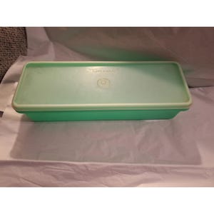 May include: A rectangular, mint green Tupperware container with a matching lid. The lid has the Tupperware logo and a circular design in the center. The container is made of durable plastic and is designed for food storage.