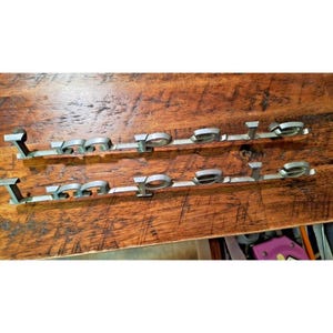 May include: Two vintage silver-toned "Polo" emblems, possibly for a vehicle, are shown on a wooden surface. The emblems are in a cursive font, with each letter individually crafted. The wood has a rich, dark brown colour.