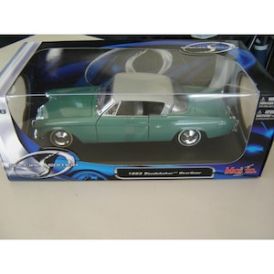 May include: A green 1953 Studebaker Starliner model car with a grey roof, presented in a clear plastic box. The model features chrome detailing and detailed wheels. The box is labelled "Special Edition" and "1953 Studebaker Starliner".