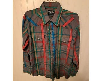 May include: Gray plaid Wrangler shirt with red, green, and blue accents. The long-sleeved shirt has two chest pockets and is hanging on a metal hanger. The Wrangler logo is visible on the collar.