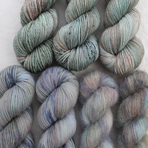 May include: Six skeins of yarn in shades of green, blue, and gray. The yarn is arranged in two rows of three skeins each. The yarn is soft and fluffy, and it would be perfect for knitting or crocheting.