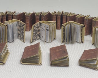 May include: A collection of miniature books with brown leather covers and gold accents. Some books are open to reveal pages with text. The books are arranged in rows on a white surface.