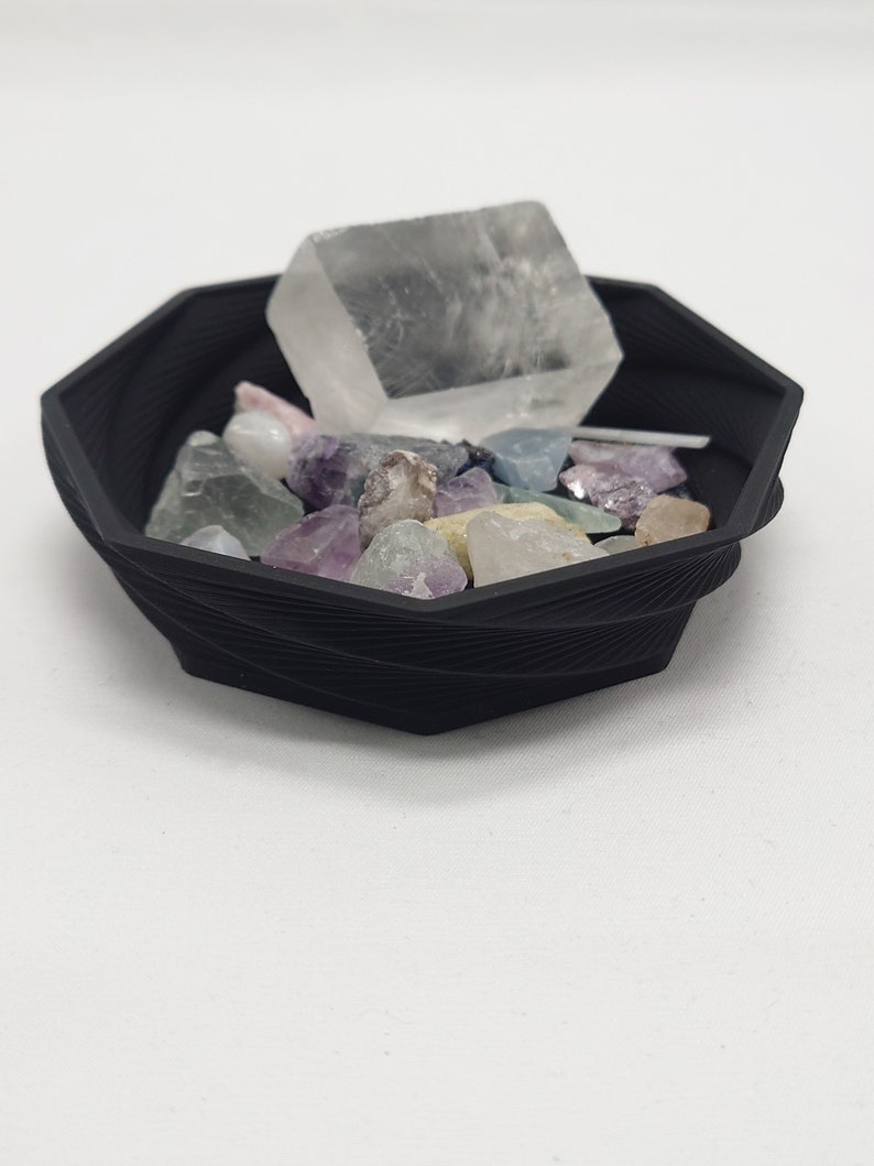 May include: A black octagonal dish with a variety of colorful crystals and a clear, cubic crystal in the center.