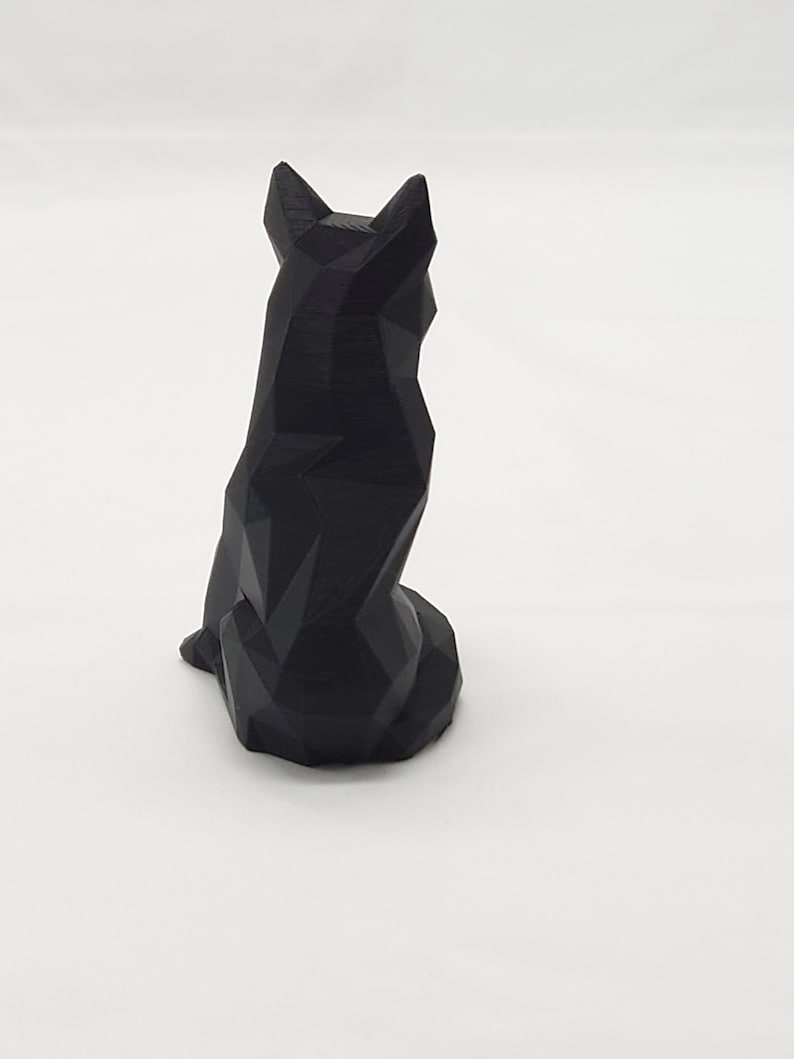 May include: A black geometric wolf sculpture. The wolf is sitting with its tail tucked between its legs. The sculpture is made of a smooth, black material.