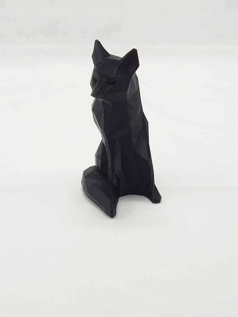 May include: A black, geometrically designed fox figurine. The fox is sitting with its tail curled around its legs.