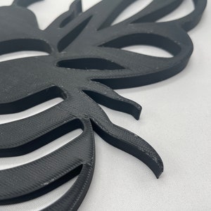 May include: Black 3D printed bee wall decor with a detailed design. The bee has a striped abdomen and wings.