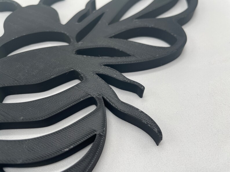 May include: Black 3D printed bee wall decor with a detailed design. The bee has a striped abdomen and wings.
