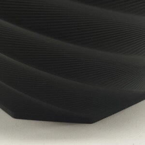 Pu&ograve; includere: Un vaso in ceramica nero testurizzato con un design a spirale organico. Il vaso ha un'apertura larga e una base stretta.