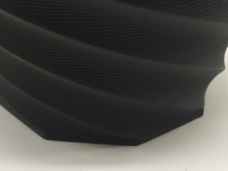 Pu&ograve; includere: Un vaso in ceramica nero testurizzato con un design a spirale organico. Il vaso ha un'apertura larga e una base stretta.