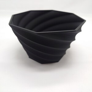 Pu&ograve; includere: Un vaso da fiori nero di forma ottagonale con un design a spirale e texture. Il vaso &egrave; realizzato in un materiale resistente ed &egrave; perfetto per aggiungere un tocco moderno a qualsiasi casa.