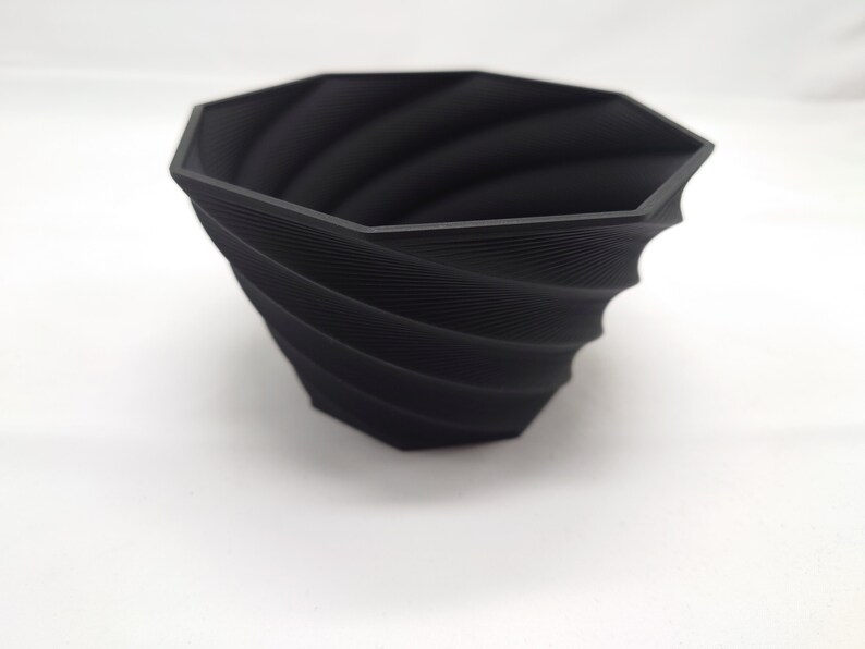 Pu&ograve; includere: Un vaso da fiori nero di forma ottagonale con un design a spirale e texture. Il vaso &egrave; realizzato in un materiale resistente ed &egrave; perfetto per aggiungere un tocco moderno a qualsiasi casa.