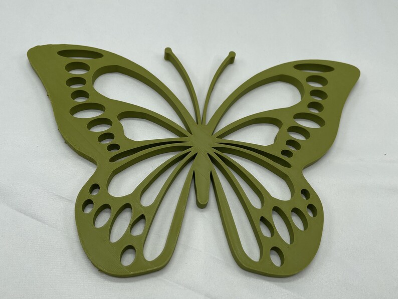 May include: A green wooden butterfly wall decor with a cutout design. The butterfly has a detailed wing pattern with multiple circles and lines.