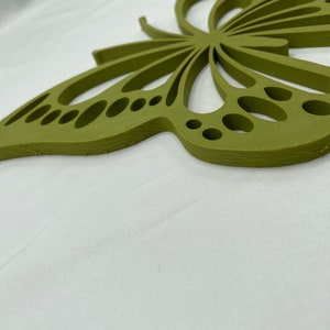 May include: A green wooden butterfly wall decor with a cutout design. The butterfly has a detailed wing pattern with small circles and a textured surface.