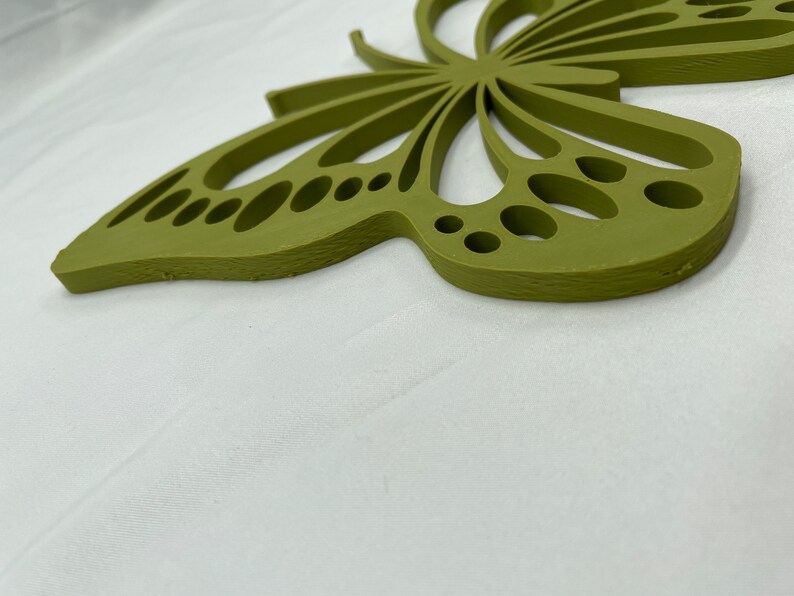 May include: A green wooden butterfly wall decor with a cutout design. The butterfly has a detailed wing pattern with small circles and a textured surface.