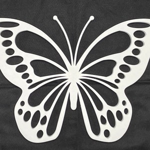 May include: White cutout butterfly wall decor with intricate details. The butterfly has a symmetrical design with a large body and wings with a pattern of circles and lines.