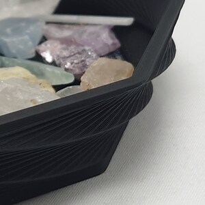 May include: A black octagonal tray with a textured, fan-like design on the rim. The tray is filled with a variety of colorful crystals.