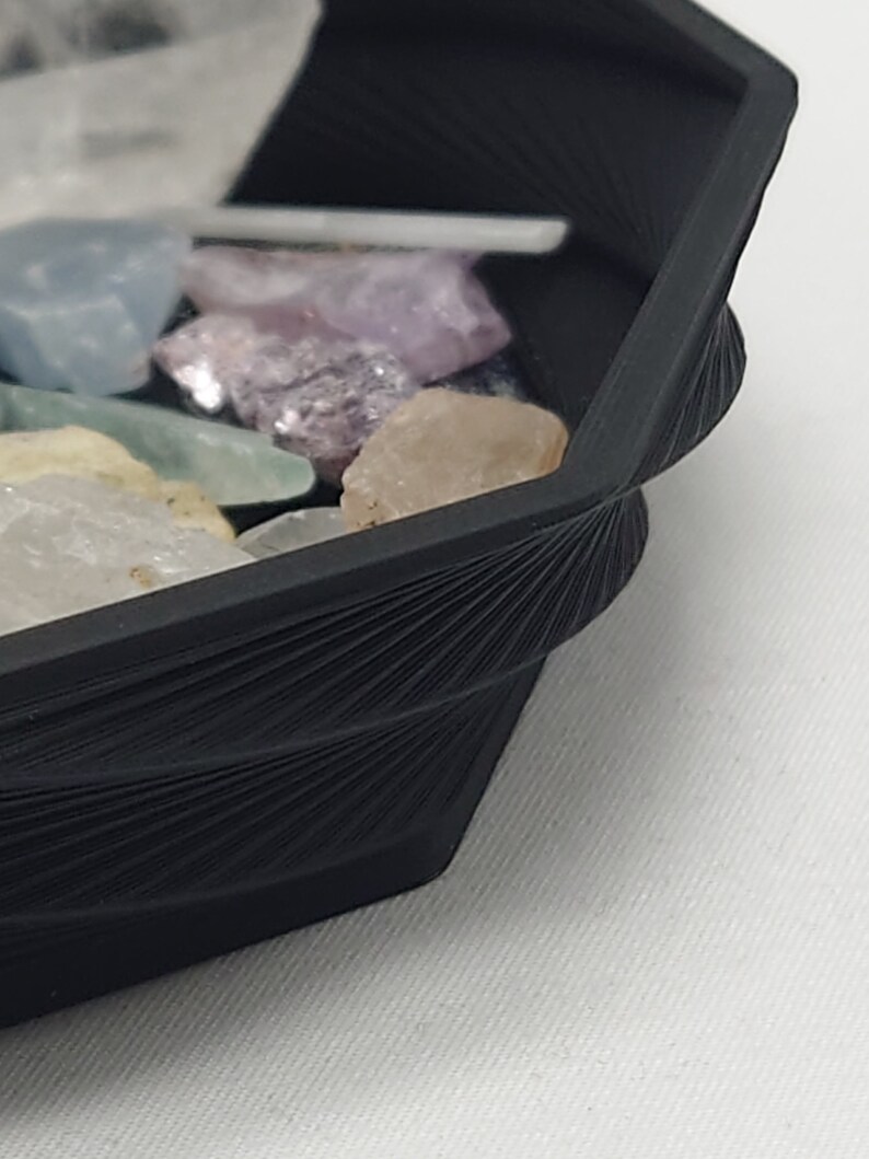 May include: A black octagonal tray with a textured, fan-like design on the rim. The tray is filled with a variety of colorful crystals.