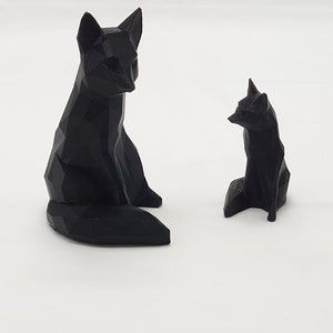 May include: Two black geometric fox figurines. The larger fox is sitting with its tail curled behind it. The smaller fox is sitting with its tail straight out behind it.