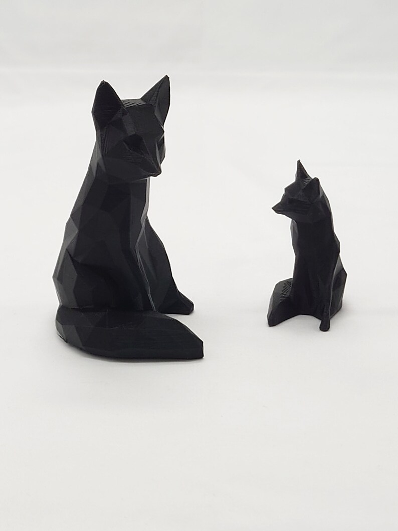 May include: Two black geometric fox figurines. The larger fox is sitting with its tail curled behind it. The smaller fox is sitting with its tail straight out behind it.