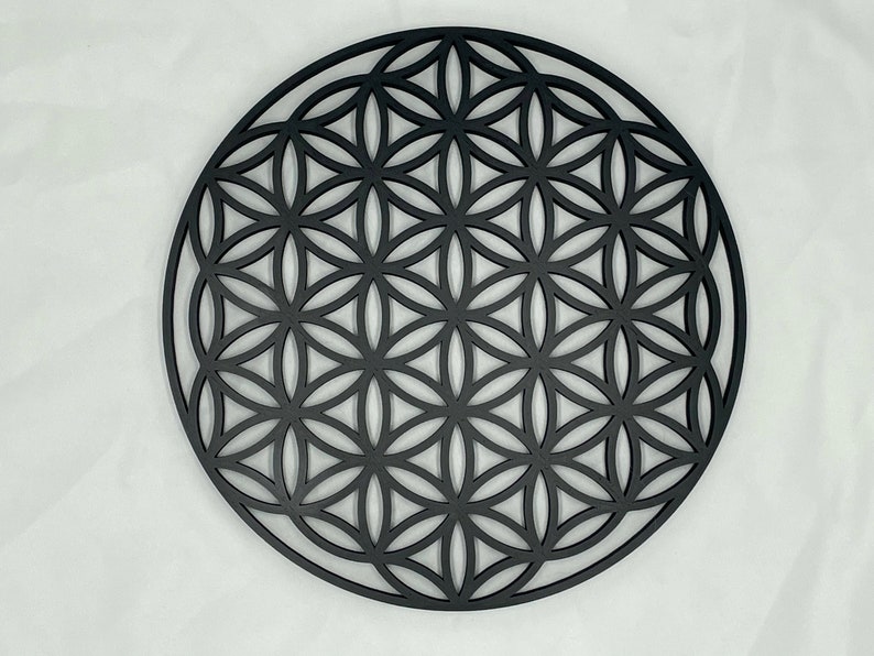 May include: A black wooden wall hanging in the shape of a flower of life mandala. The intricate design features overlapping circles and geometric patterns.