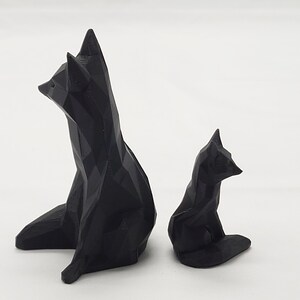 May include: Two black geometric fox sculptures, one larger than the other, are sitting on a white surface. The sculptures are made of a 3D printed material.