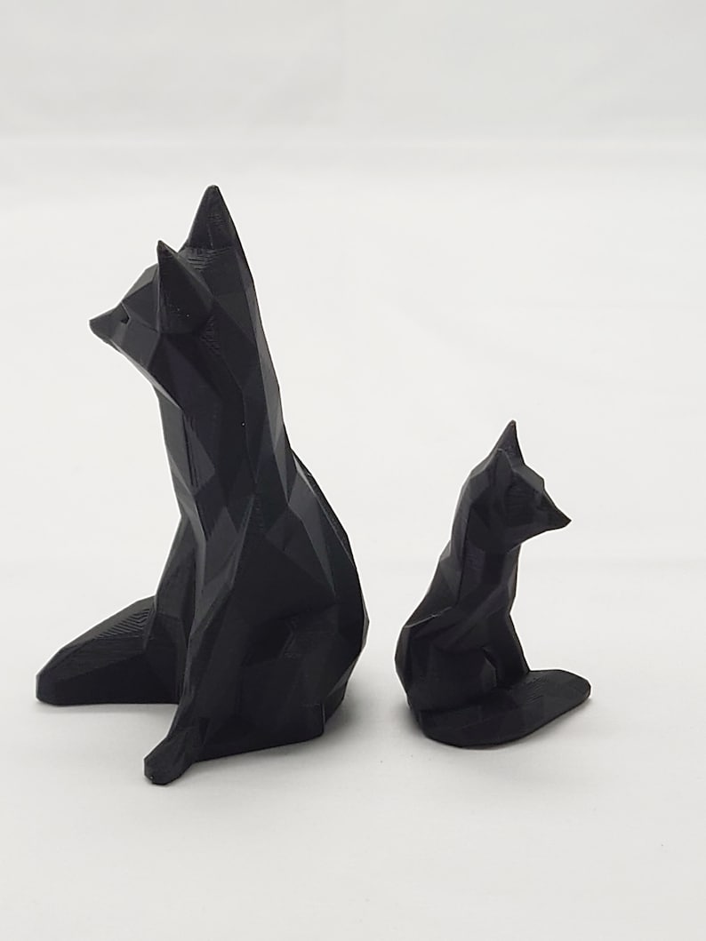 May include: Two black geometric fox sculptures, one larger than the other, are sitting on a white surface. The sculptures are made of a 3D printed material.