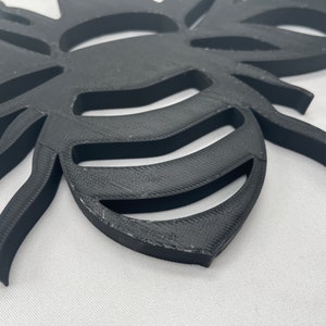 May include: A black 3D printed bee cutout with a detailed design. The bee has a segmented body and wings, and the wings are cut out to create a decorative effect.