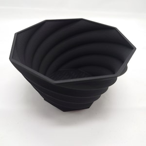 Pu&ograve; includere: Un vaso da fiori nero di forma ottagonale con un design a spirale e texture. Il vaso &egrave; realizzato in un materiale resistente e ha un'ampia apertura.