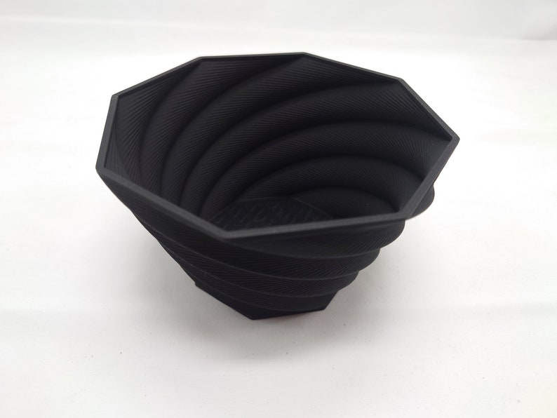 Pu&ograve; includere: Un vaso da fiori nero di forma ottagonale con un design a spirale e texture. Il vaso &egrave; realizzato in un materiale resistente e ha un'ampia apertura.