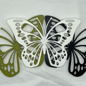 May include: Three decorative butterfly cutouts in green, white, and black. The butterflies are layered on top of each other.