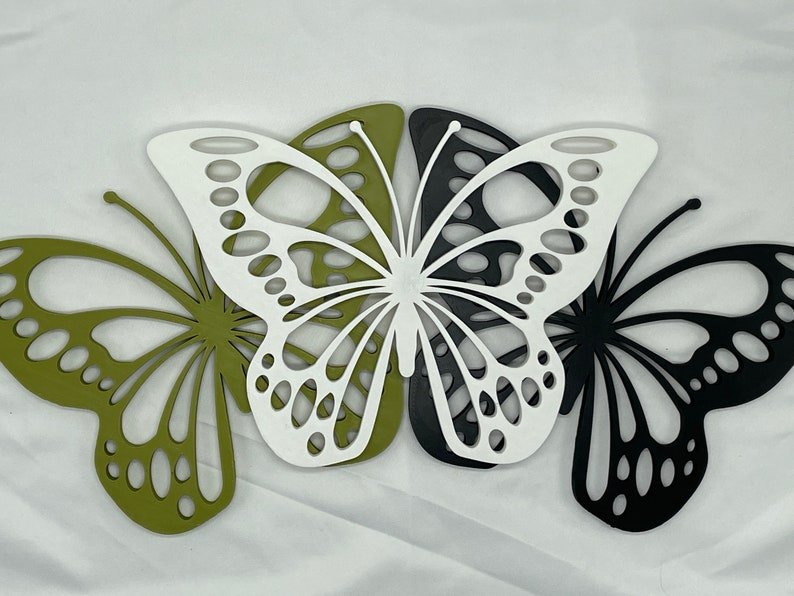 May include: Three decorative butterfly cutouts in green, white, and black. The butterflies are layered on top of each other.