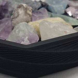 May include: A close-up of a black hexagonal tray filled with various colorful gemstones. The tray is made of a woven material and has a smooth, polished finish.