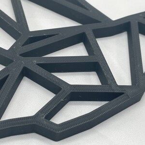 May include: A close-up of a black geometric wall decor made of 3D printed plastic. The design features a series of interconnected triangles, creating a modern and abstract look.