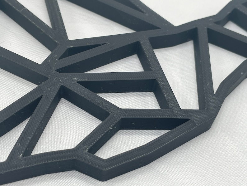 May include: A close-up of a black geometric wall decor made of 3D printed plastic. The design features a series of interconnected triangles, creating a modern and abstract look.