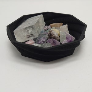 May include: A black octagonal bowl filled with a variety of colorful crystals and a large clear crystal.