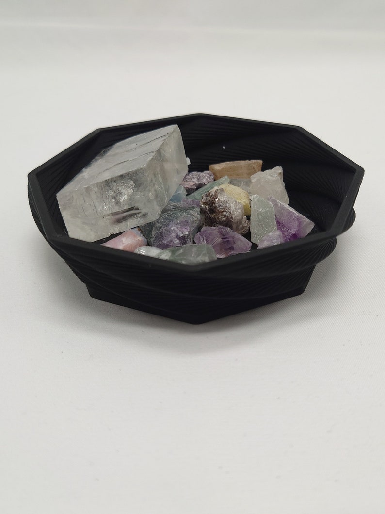 May include: A black octagonal bowl filled with a variety of colorful crystals and a large clear crystal.