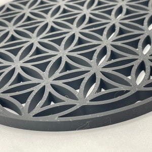 May include: A gray, circular, decorative object with a geometric pattern of overlapping circles and triangles. The pattern is reminiscent of a flower of life design.