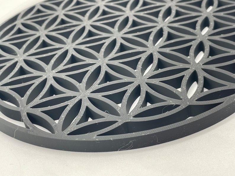 May include: A gray, circular, decorative object with a geometric pattern of overlapping circles and triangles. The pattern is reminiscent of a flower of life design.