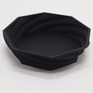 May include: A black octagonal bowl with a textured, swirling design. The bowl is made of a smooth, hard plastic.