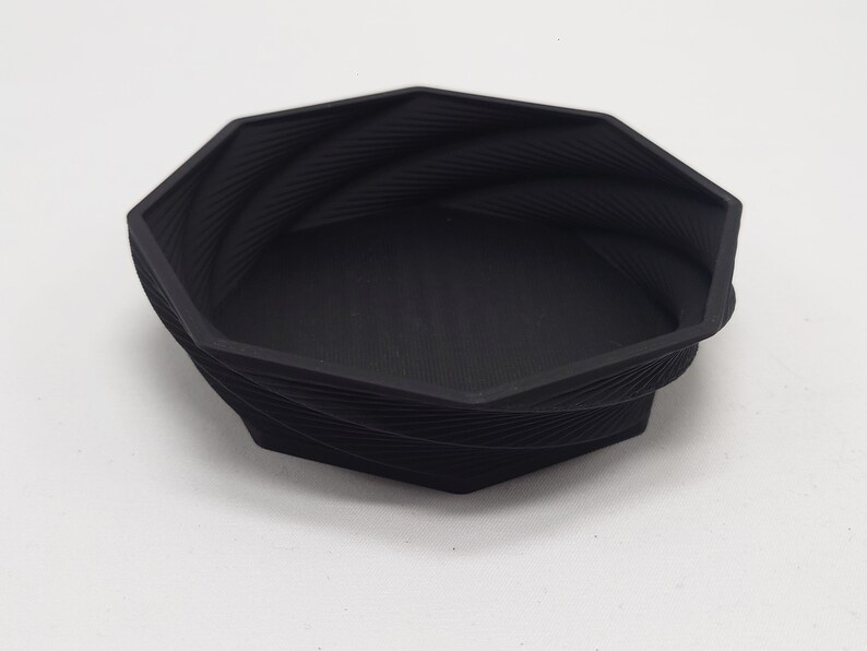 May include: A black octagonal bowl with a textured, swirling design. The bowl is made of a smooth, hard plastic.