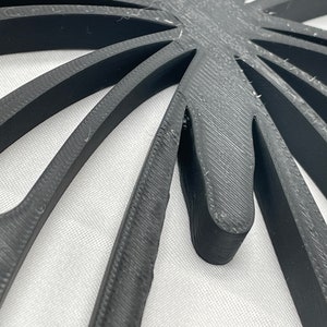 May include: Close-up of a black, 3D printed, geometric design with a starburst pattern. The design has a textured surface and appears to be made of plastic.