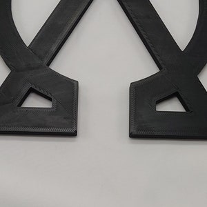 May include: Two black 3D printed pieces that are shaped like a letter X. The pieces are connected at the top and bottom, forming a symmetrical shape.