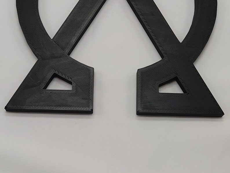 May include: Two black 3D printed pieces that are shaped like a letter X. The pieces are connected at the top and bottom, forming a symmetrical shape.