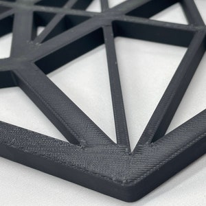 Pu&ograve; includere: Un decoro da parete geometrico nero realizzato in plastica stampata in 3D. Il design presenta un motivo ripetitivo di triangoli e quadrati.