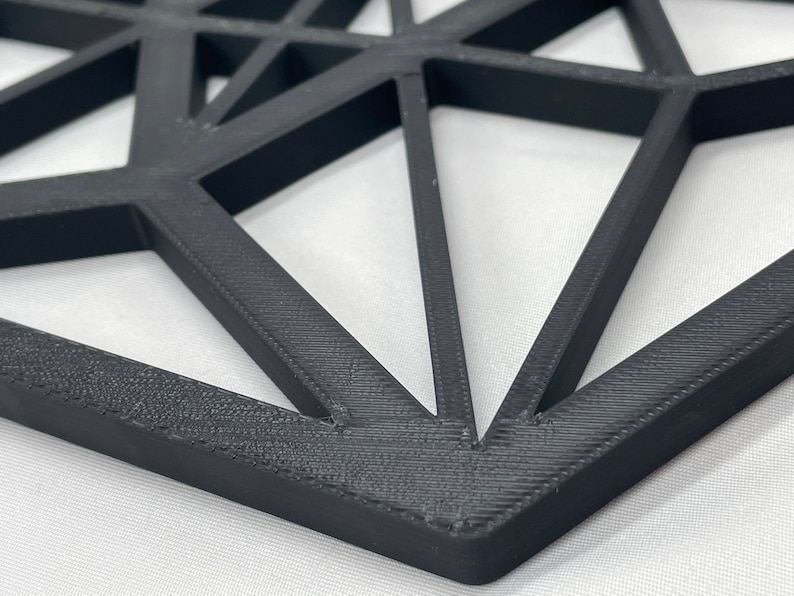 Pu&ograve; includere: Un decoro da parete geometrico nero realizzato in plastica stampata in 3D. Il design presenta un motivo ripetitivo di triangoli e quadrati.