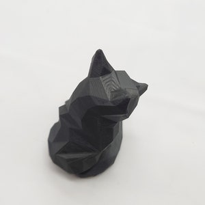 May include: A black, geometrically shaped cat figurine. The cat is sitting with its head tilted to the side.
