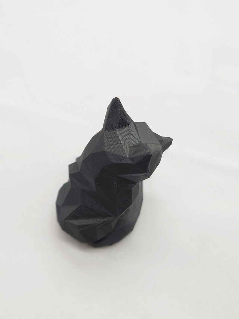 May include: A black, geometrically shaped cat figurine. The cat is sitting with its head tilted to the side.