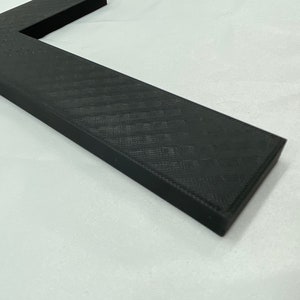 May include: A black cross made of a textured material. The cross is lying on a white surface.